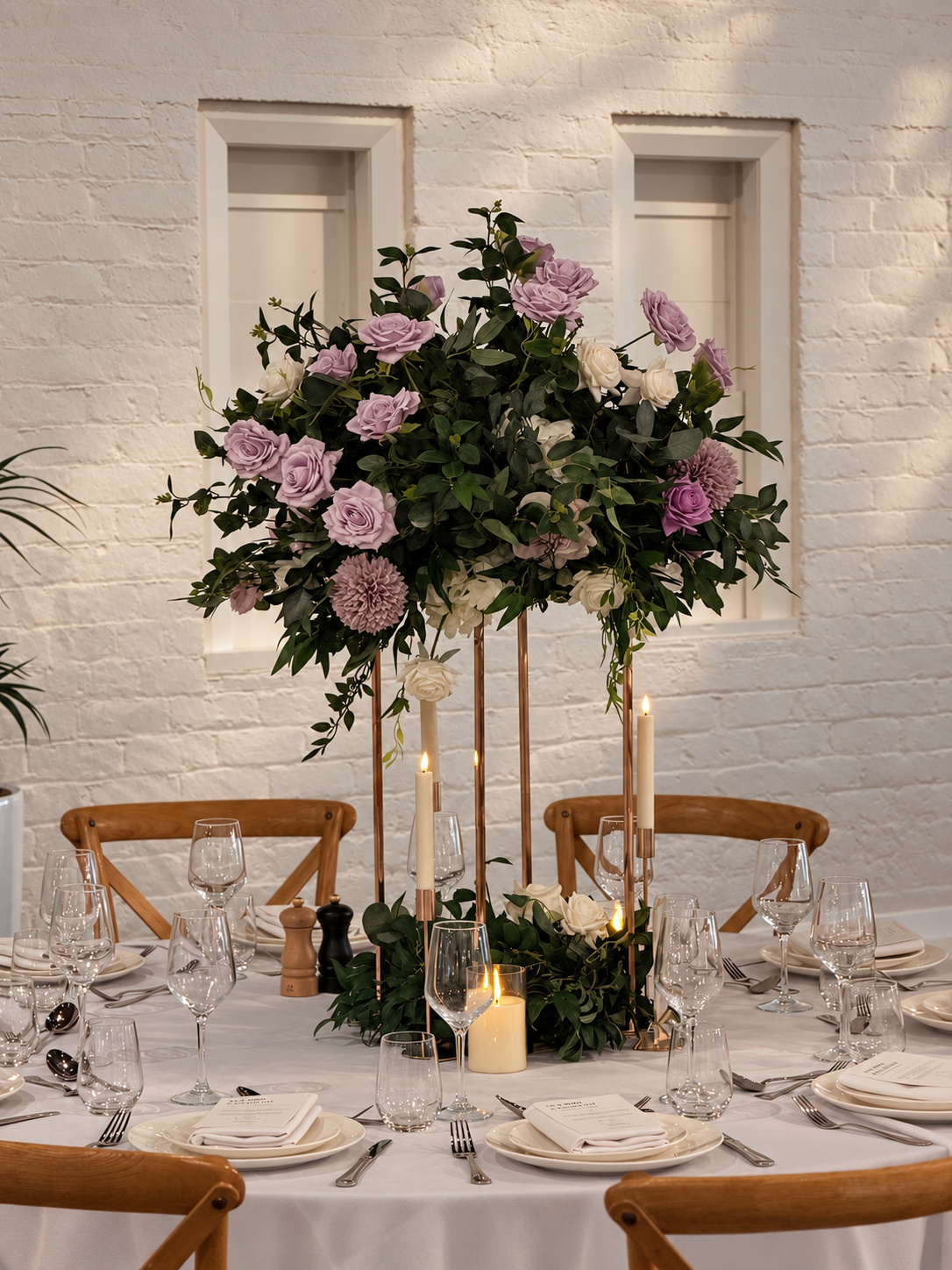 Elegant wedding reception styling with tall lilac, ivory and white floral centrepieces, lush greenery, candlelight and refined table decor.