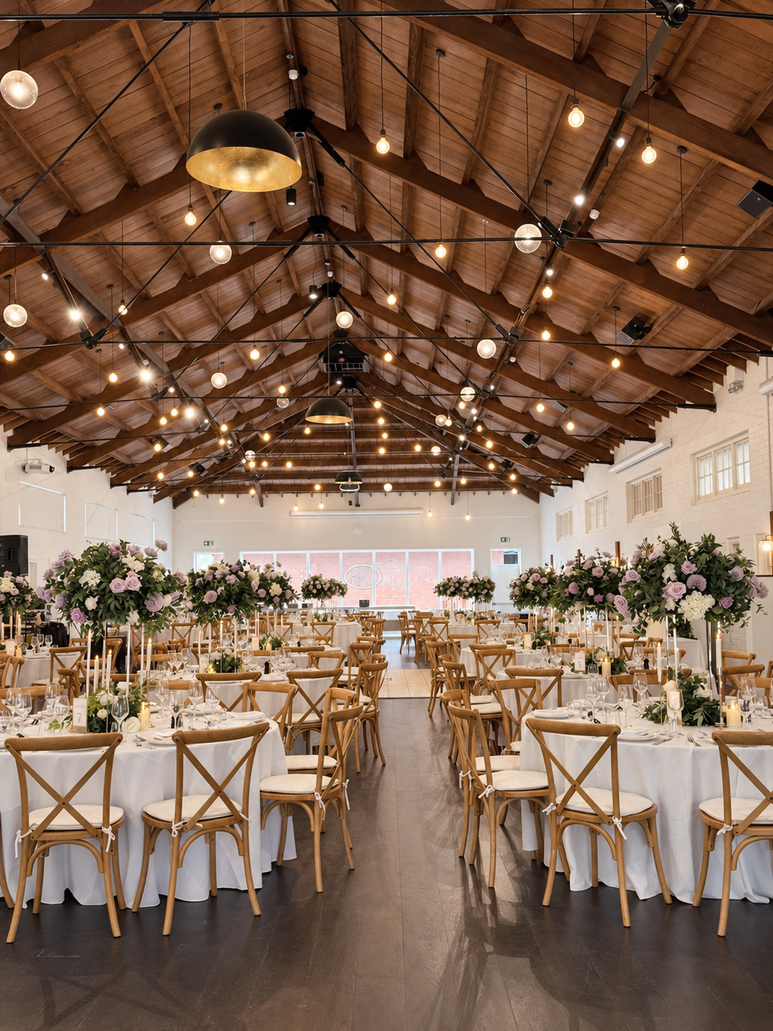 Elegant wedding reception styling with tall lilac, ivory and white floral centrepieces, lush greenery, candlelight and refined table decor.
