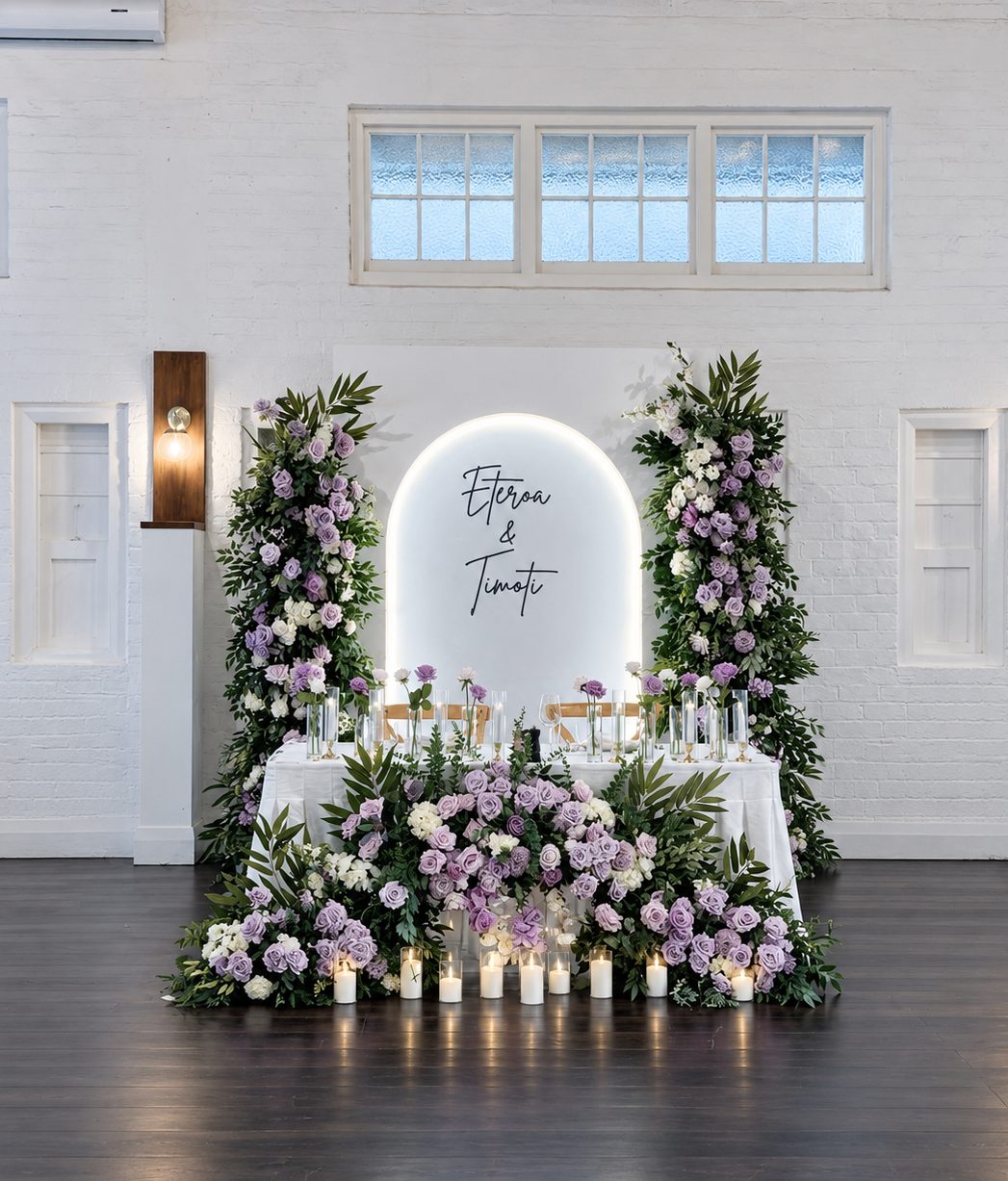Luxury Breanna 3D arch bridal table backdrop with lilac and white florals, personalised names, floor flowers and LED candles for an Auckland wedding.